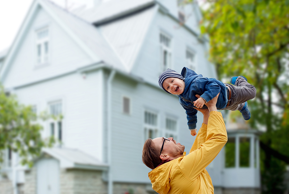 Father holding up his son in front of a historic style home.