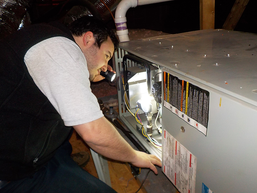 One of Foundations' home inspectors Kalebh Withers inspecting a piece of equipment with a flashlight.