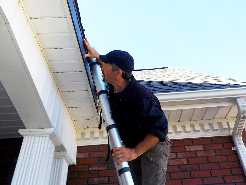 One of Foundations' home inspectors Dayne Withers on a ladder inspecting a roof.