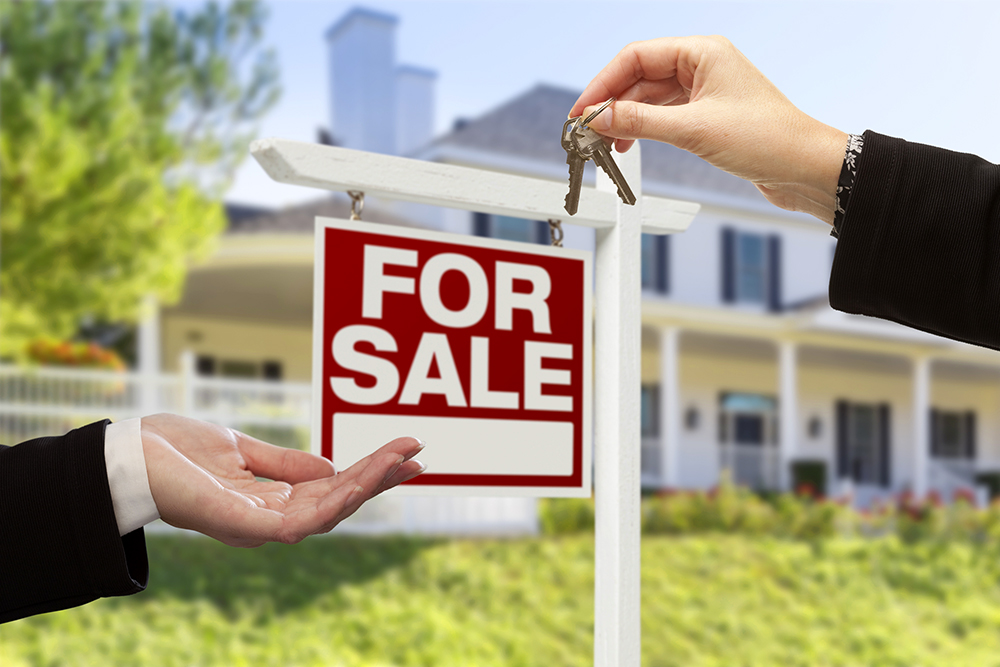 Real Estate Agent Handing Over the House Keys in front of a For Sale sign